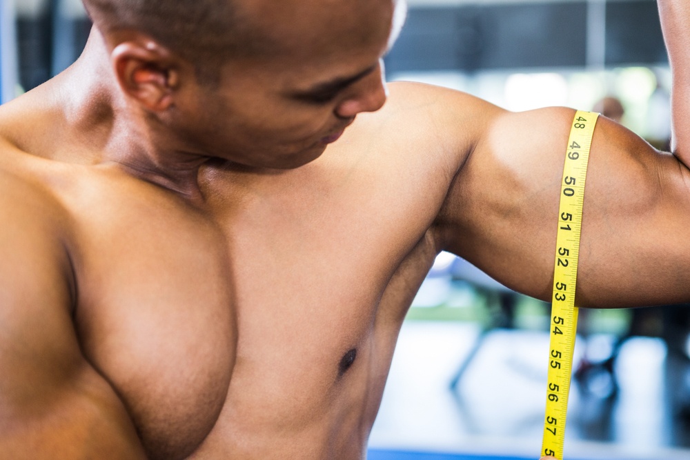 Close-up of muscular man measuring biceps with tape measure in gym.jpeg