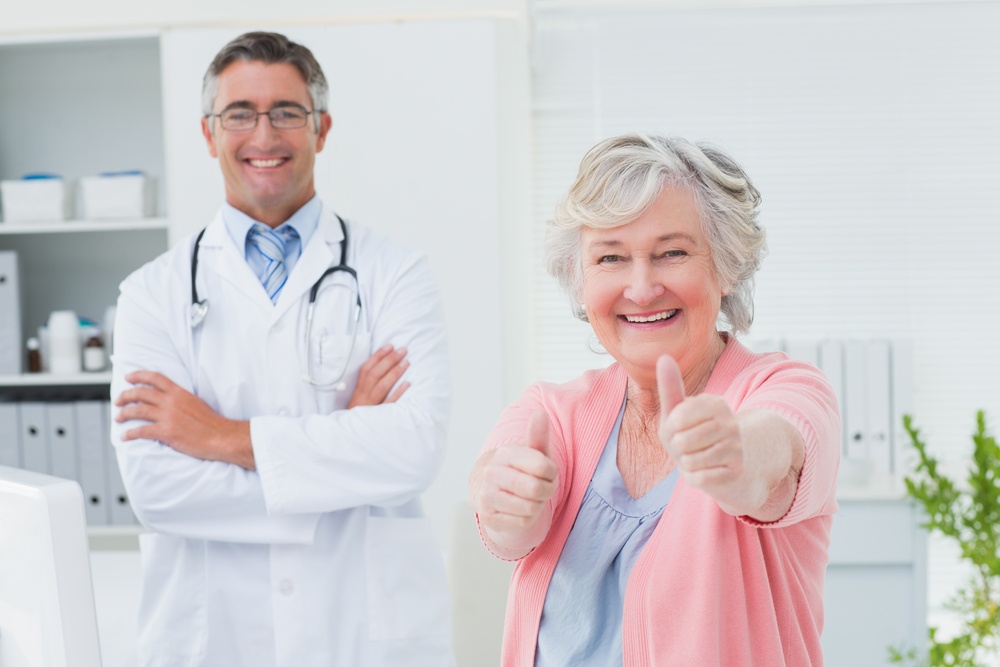 Portrait of happy female patient showing thumbs up sign while standing with doctor in clinic.jpeg