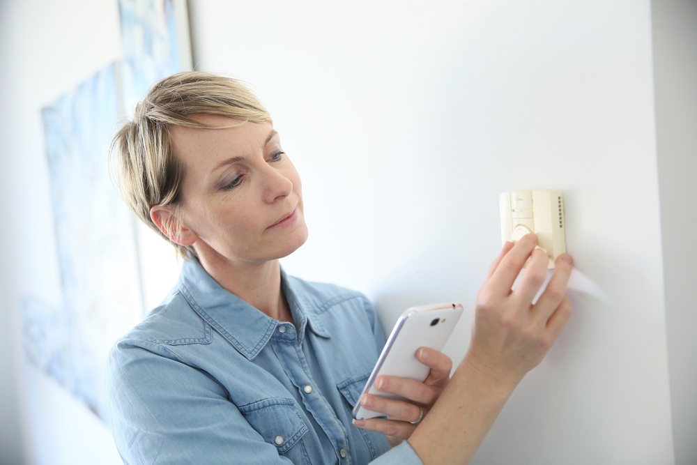 Woman porgramming indoor temperature with smartphone application.jpeg